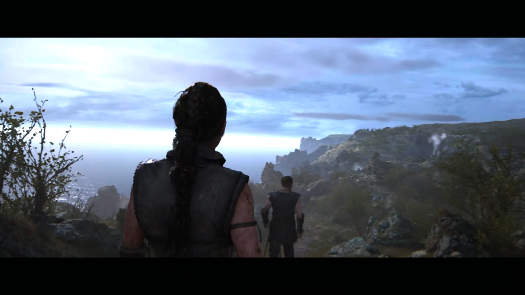 Senua walks behind companion on coastal cliff path