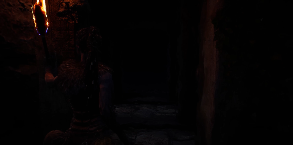 Person holding torch in dark cave corridor