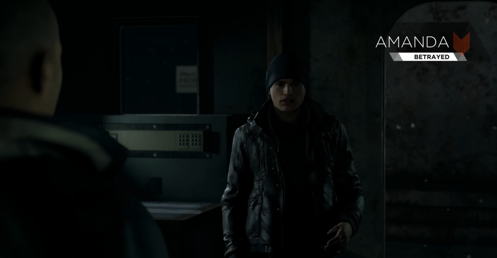 Amanda stands in dark room, wearing black jacket