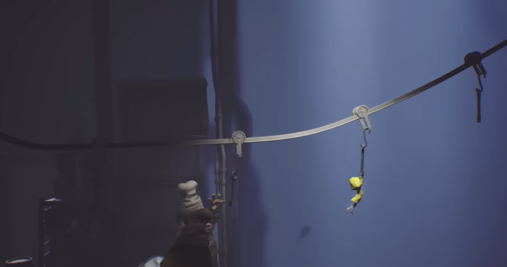 Little Nightmares character hangs from cable in blue room