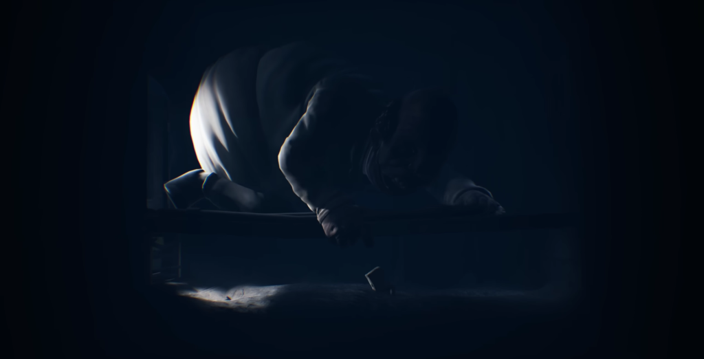 Person crouching beside bed in dark room